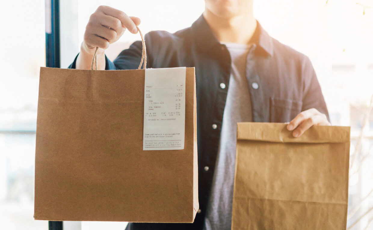 A person delivering two food takeout orders in brown paper bags