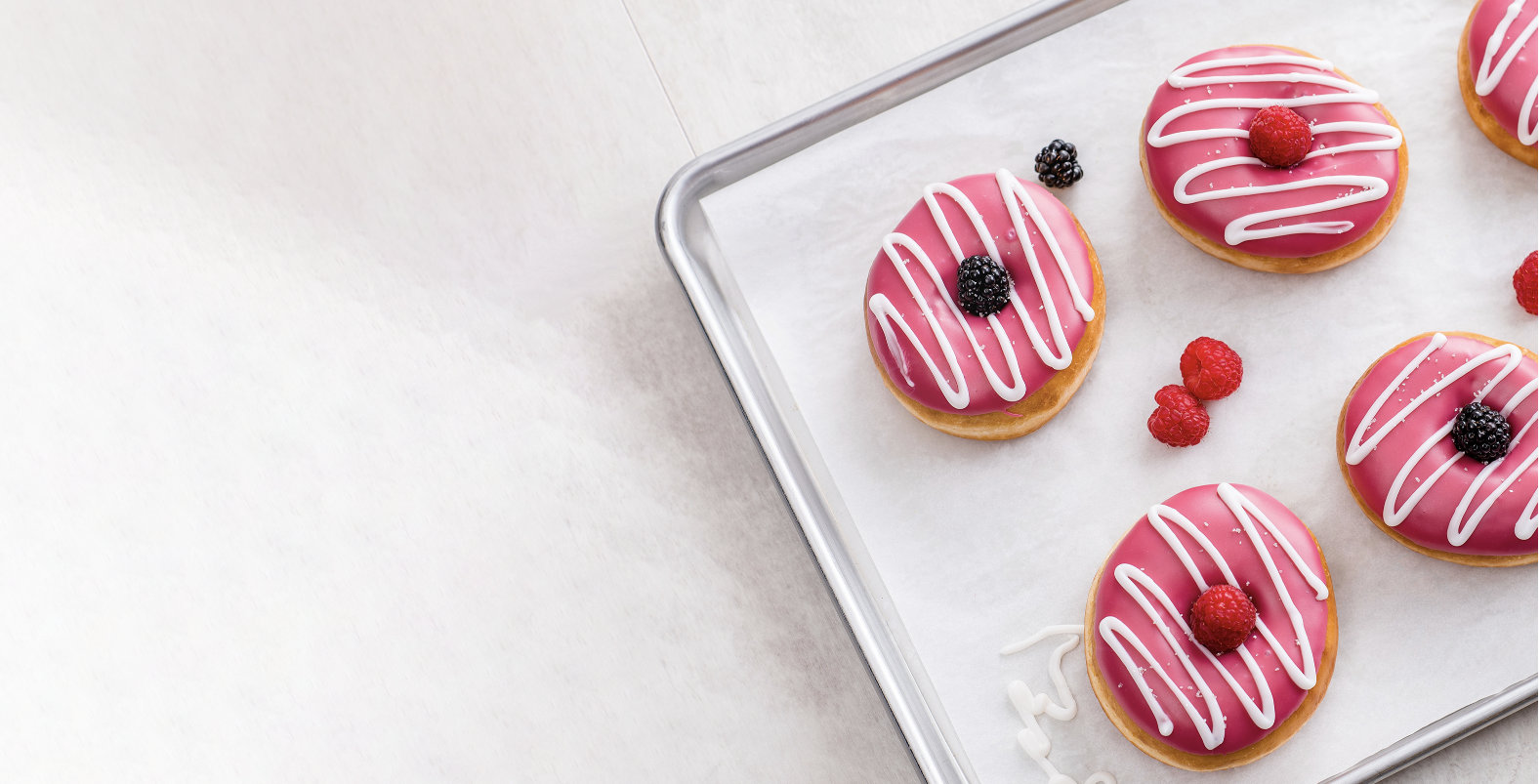 Donuts with pink and white icing garnished with berries on a baking sheet