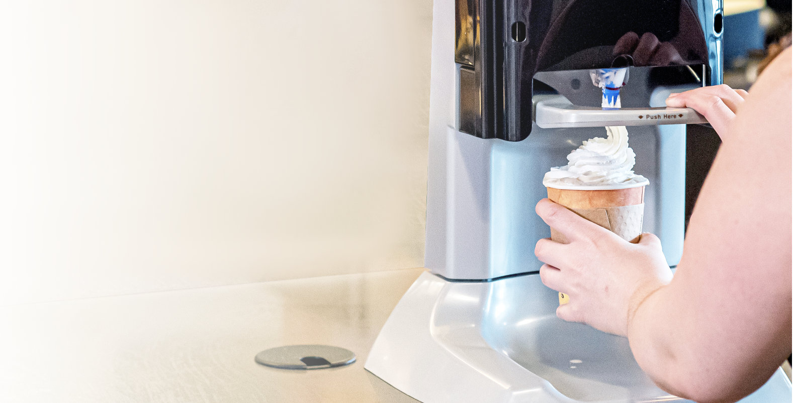 Person using a machine to apply whipped topping onto a drink