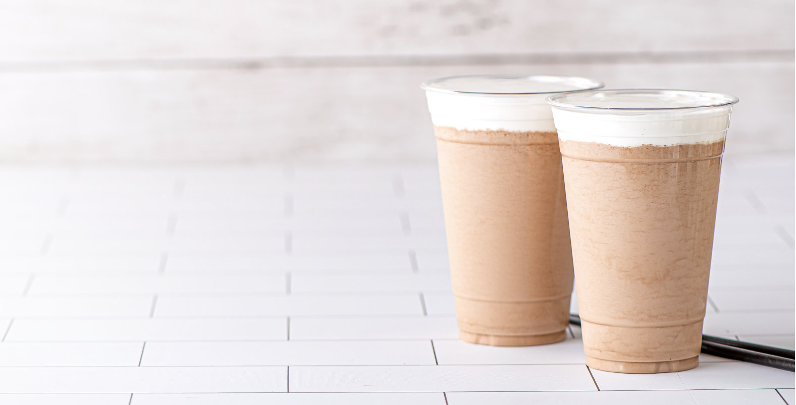 Two cups filled with drinks with a whipped topping and straws in the background