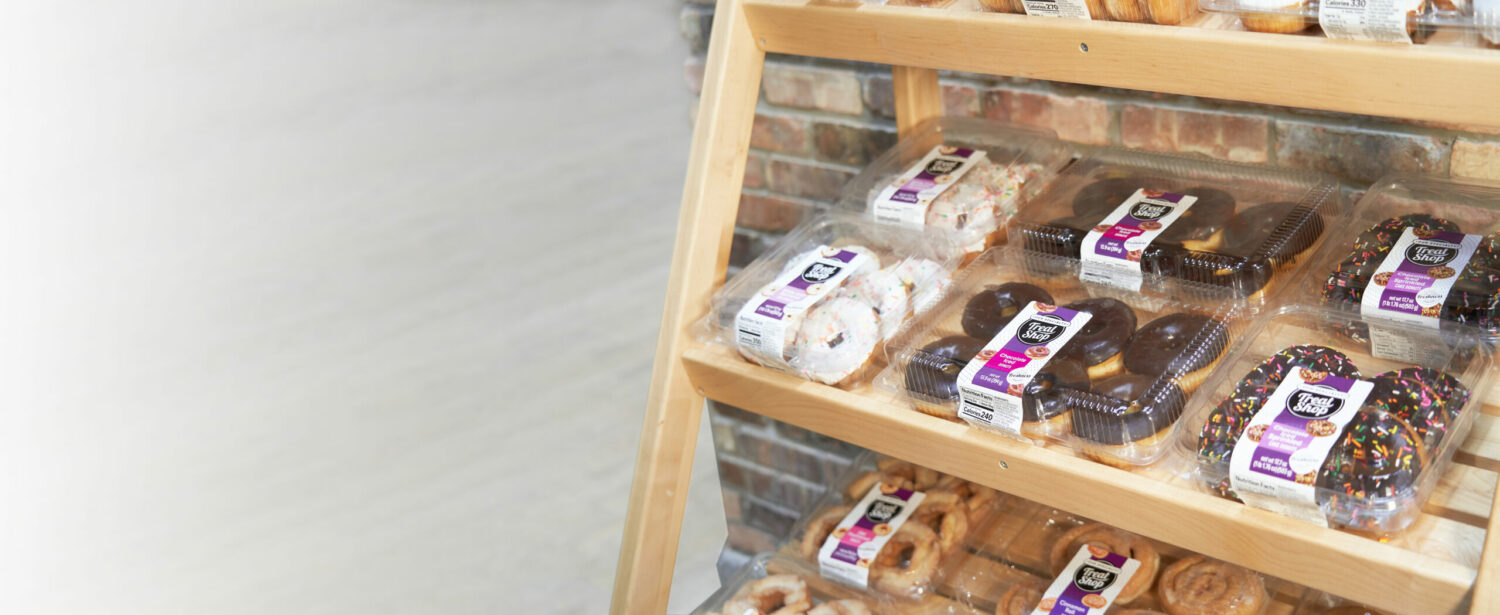 Wooden shelf with multiple packages of Our Speciality Bake Shop donuts and desserts