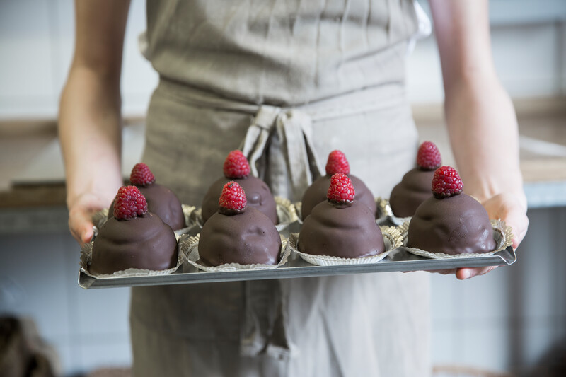 Person holding chocolate cookies with raspberries on tray