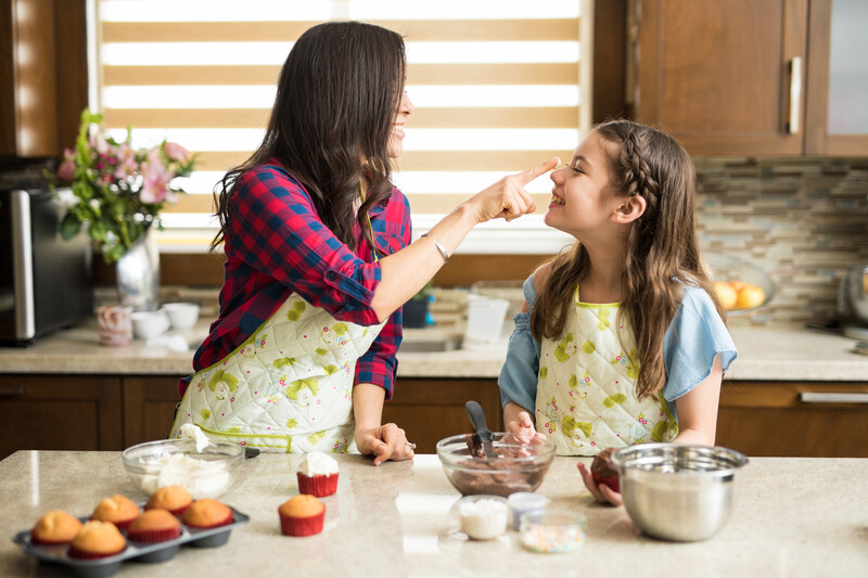 Profile view of a cute girl having fun with her mom in the kitchen while baking and decorating cupcakes with frosting